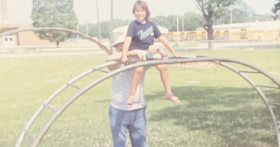 Dom, about 10 or 11 years old, is on a jungle gym with their grandfather standing behind them.